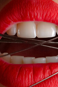 A close-up photo of a woman wearing red lipstick with gray cables across her mouth