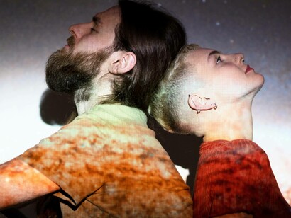 Un uomo e una donna sono seduti schiena contro schiena, entrambi illuminati da una proiezione stellare