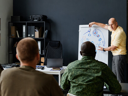 Military trainer presenting battlefield tactics using a whiteboard with hand-drawn sketches and operational arrows