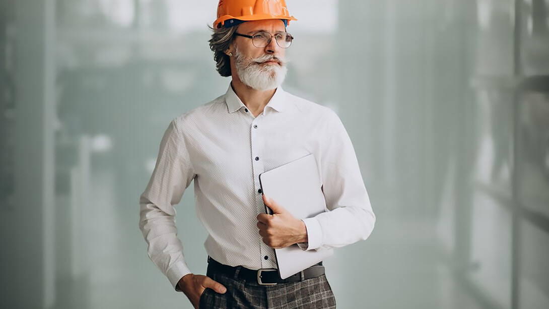 An elderly businessman wearing a hard hat, demonstrating the active role of senior professionals in industries requiring hands-on involvement