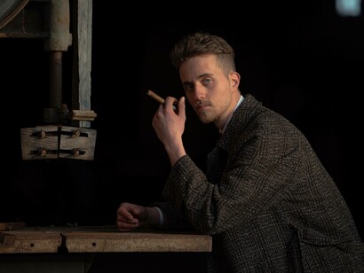A man fashionably dressed in a tweed coat holding a cigar