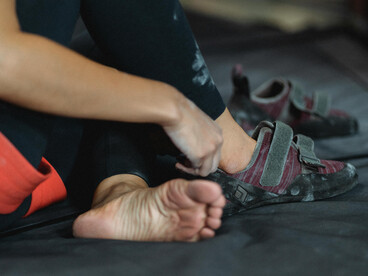 A cropped image of a woman lacing up her sneakers, getting ready for a bouldering climb