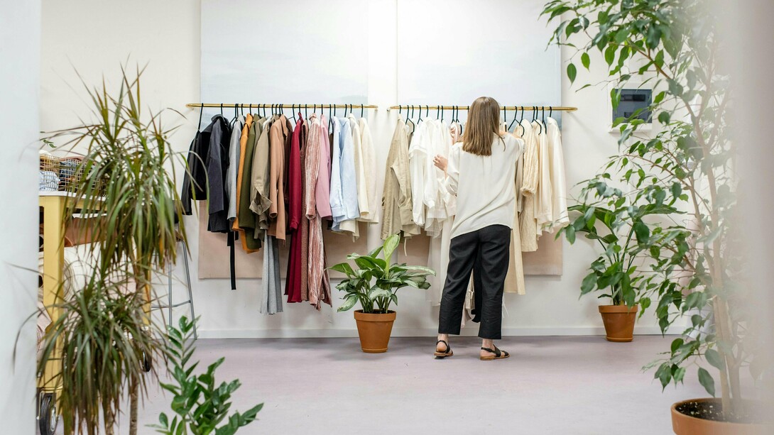 Mulher escolhe roupas em uma arara de loja. Mais do que estilo, cada escolha revela valores e um novo olhar sobre o consumo consciente. Entre peças e possibilidades, a decisão vai além da estética. Consumir moda hoje também é um ato de responsabilidade
