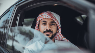 A man in a white long-sleeve shirt, wearing a red and white hijab, sitting inside a car