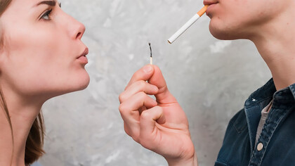 Close-up of a woman blowing on a matchstick held by her boyfriend, who has a cigarette in his mouth, with an intimate and casual vibe