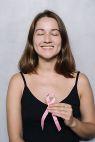 A woman wearing a black spaghetti strap top holds a pink ribbon, symbolizing breast cancer awareness