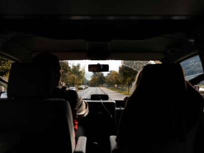 The road ahead is framed by the interior of the vehicle, reinforcing that travel is not just about the destination but about the continuous act of moving through space with awareness

