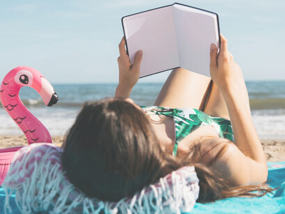 A woman enjoying a book at the beach with her friend, embracing a holiday digital detox amidst nature and travel