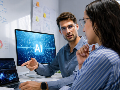 Two programmers discussing an artificial intelligence project while working on a laptop in a modern home office at night