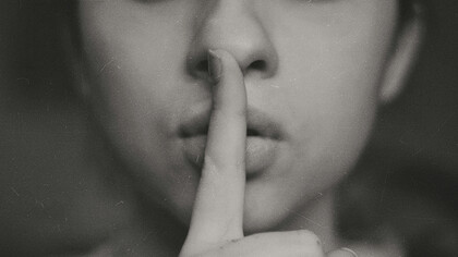 Close up of a woman's index finger pressed against her mouth, calling for quietness