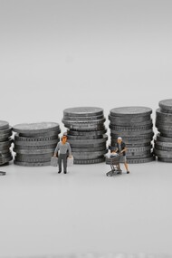Miniature di consumatori con carrelli della spesa davanti a pile di monete: una rappresentazione simbolica del rapporto tra consumo, denaro e potere d'acquisto