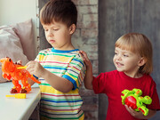 Duas crianças brincam uma ao lado da outra com dinossauros de brinquedo