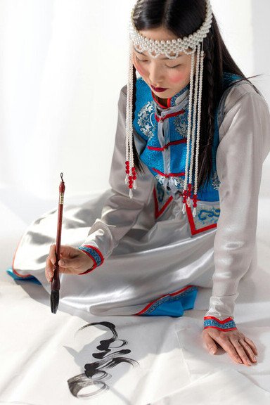 Imagem de pessoa em traje oriental tradicional, concentrada na caligrafia com pincel, explorando a arte como forma de expressão