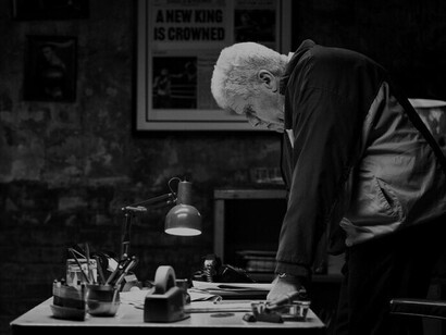 Stevie, portrayed by Ron Perlman, stands in his office, deep in thought, reflecting on the weight of the responsibility he holds as Mike Flannigan's trainer, knowing the crucial role he plays in his fighter’s journey to redemption