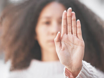 A photograph of an unidentified woman making a stop gesture with her hand outdoors