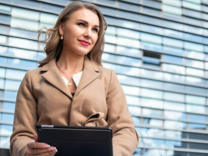 A businesswoman using a digital tablet outside a sleek office building, representing the empowerment of women in the economy