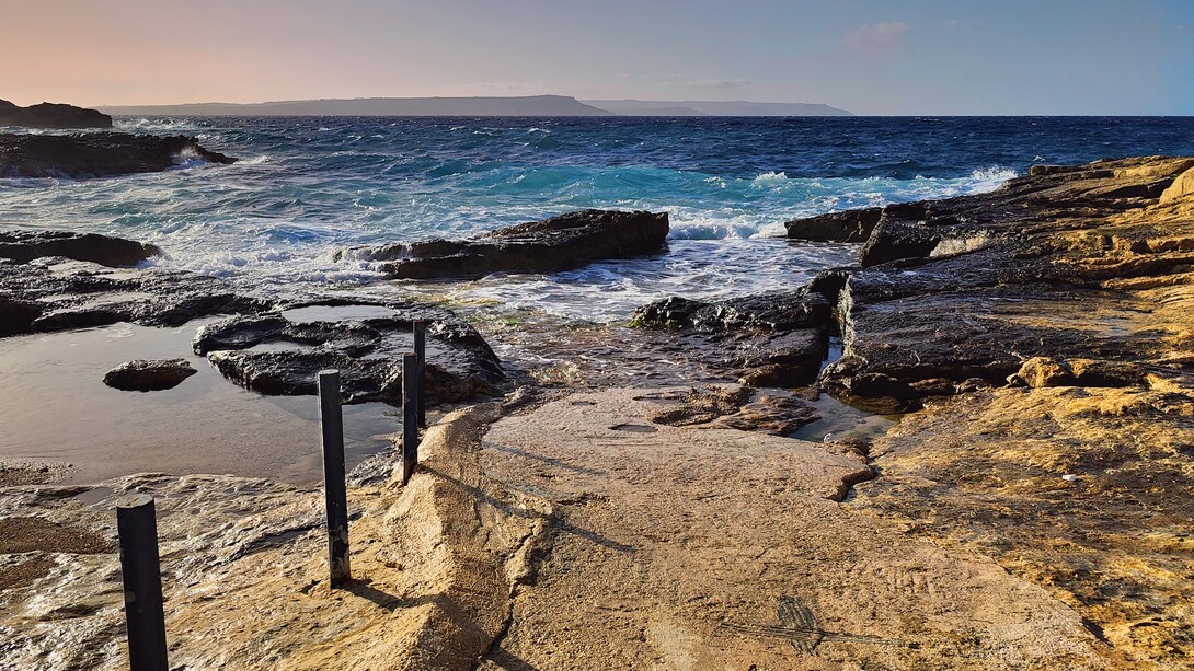 Foto tomada desde ix-Xatt l-Ahmar en la isla de Gozo. El lado occidental de la isla de Malta se puede ver a lo lejos, al otro lado del canal entre las dos islas. Mares agitados y la hermosa textura de las rocas maltesas. Invierno de 2024, Gozo, Malta