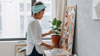 A woman arranging images and ideas on a vision board, representing the process of designing a self-care routine around personal needs and desires