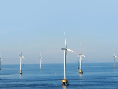 An aerial view of offshore wind turbines at sea under a clear blue sky, representing carbon-neutral, clean energy and sustainable alternative technology