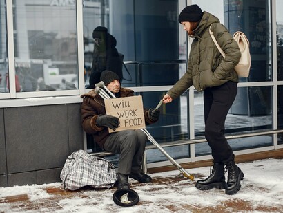 A homeless man receiving a donation from a passerby, reflecting the economic barriers that prevent access to basic necessities