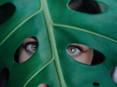 Ragazza con gli occhi verdi guarda attraverso delle foglie verde scuro