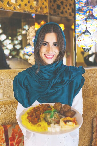 A woman presenting a dish of Chelo Kebab, a hallmark of Iranian cuisine