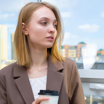 A woman in a brown blazer holds a cup of coffee while thinking quietly