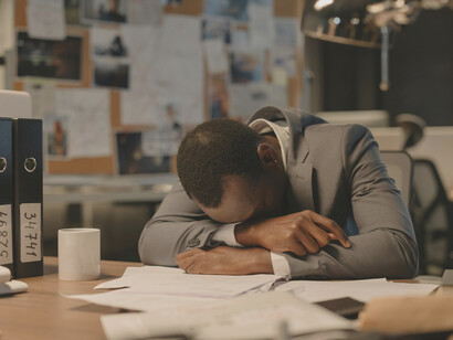 A man stays late in his office, working through an overload of paperwork and folder