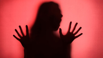 A silhouette of a woman stands gracefully behind flowing red curtains