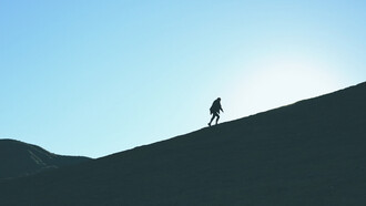 Mujer caminando cuesta arriba hacia la cima de una montaña. Para este 2023, haz que tus sueños vuelen, incluso más allá de lo que visualizas