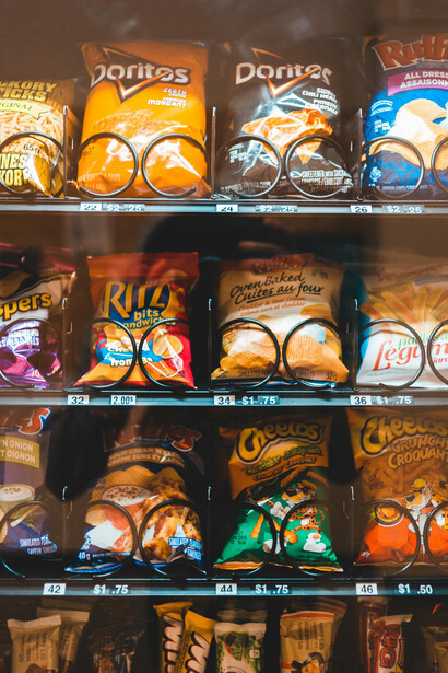 Shelves filled with brightly colored snack packages in a vending machine, featuring crisps and other ultra-processed treats