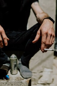 A person sitting on a step with a can and a cigarette 