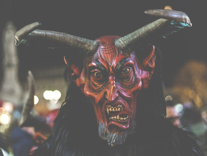 Krampus con una maschera lignea, alte corna arcuate, denti aguzzi e una rossa lingua adunca