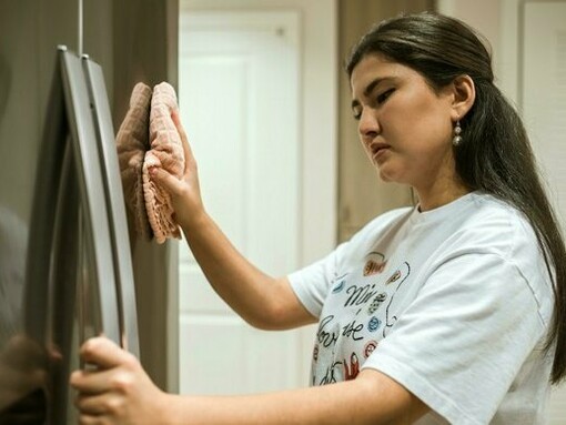 A woman cleaning her fridge thoroughly, echoing the need for monthly deep-cleaning