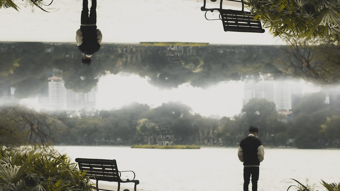 A man standing in front of a park bench, creating an optical illusion that distorts perception
