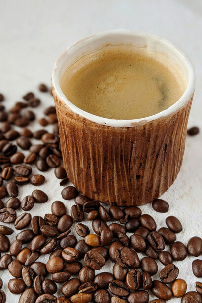 A textured brown cup filled with coffee, nestled among dark roasted beans