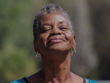 An elderly woman practicing deep breathing exercises in a peaceful forest, connecting with nature