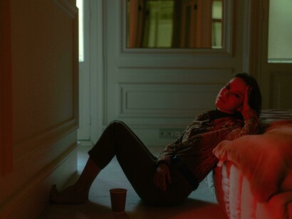 A woman leans on her bed in a dimly lit room, captured in a moment of silence and introspection