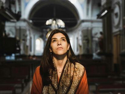 Woman in an orange long-sleeve shirt holding a black Bible and praying inside a church