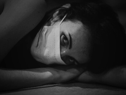 A person resting their head on a desk while wearing a mask