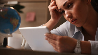 A young woman at work reacting with sadness as she reads on her touchpad