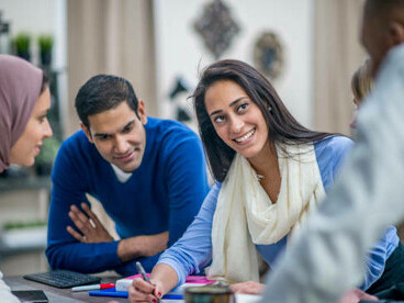 A diverse group of young entrepreneurs, including a migrant wearing a turban, collaborate in a vibrant workspace