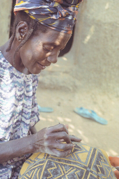 Ill. 48. Salimata Kone painting the “foot of the dove” (ntufan sen) motif in the center of a cloth decorated with the “Town gate” (Kalanga da) pattern. She is using a metal spatula. Kolokani, 7/5/78.  
Photocredit Sarah C. Brett–Smith
