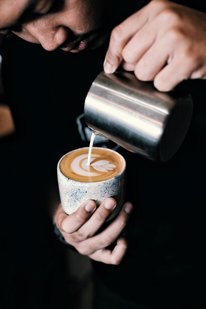At a trendy startup café, a person carefully pours milk into a cup of coffee