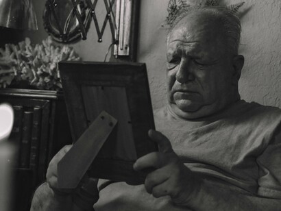 Homem segura um porta-retrato enquanto observa a fotografia com expressão de saudade. As lembranças de quem amamos continuam presentes mesmo quando precisamos aprender a conviver com a ausência