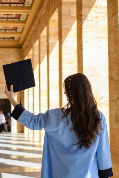 A brunette woman holds her graduation hat thoughtfully, embodying the bittersweet transition from student life to the wider world
