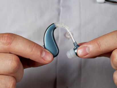 A doctor carefully holding a modern hearing aid between their fingers, representing the integration of connected medical devices with the human body