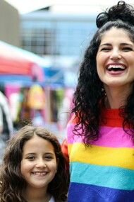 A woman in a rainbow sweatshirt with her child, symbolizing a queer family