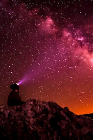 A striking silhouette photograph captures a person holding a flashlight against the backdrop of the Milky Way, evoking the enchanting beauty of the night sky