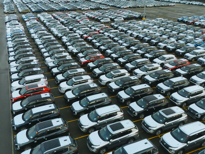 Aerial view of thousands of cars lined up in a vast parking lot, reflecting global auto production